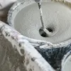 A close-up view of a mixing paddle stirring a thick, gray mixture in a bucket. Anteprima dell’immagine prodotto