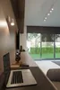 A modern home office setup with a laptop, headphones, and a view of a garden through large windows. Produktbild-Vorschau