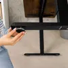 A person's hands are shown adjusting a component on the leg of a standing desk. Náhled obrázku produktu