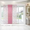 Panel curtains with a pink and white floral pattern are installed on a sliding glass door, looking out onto a garden. Produktbild-Vorschau