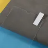 A close-up shot of a transparent screen protector with a white tab on a textured gray surface, with a blue and yellow background visible. Produktbild-Vorschau
