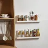 Two white shelves mounted on a white wall, displaying kitchen items like spice jars, utensils, and bottles of condiments. A wooden cabinet is visible on the left side. Anteprima dell’immagine prodotto