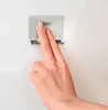 A hand is pressing on a silver wall-mounted holder for a shower squeegee. Produktbild-Vorschau