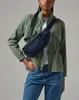 A person wearing a green jacket and blue jeans, with a navy blue fanny pack across their chest. Anteprima dell’immagine prodotto