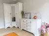 A white corner wardrobe and a white dresser with decorative items are shown in a room. Náhľad obrázku produktu