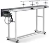 A long, silver conveyor belt system with a black belt, supported by a metal frame, is shown against a white background. A black motor is attached to the left end of the conveyor belt. Náhled obrázku produktu
