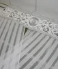 A close-up view of the top portion of a white striped curtain with a decorative silver band and a white laser-cut overlay. Náhľad obrázku produktu