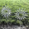 Two silver kinetic wind sculptures are displayed in a grassy outdoor setting. Anteprima dell’immagine prodotto