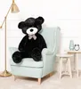 A large black teddy bear sits in a light blue armchair, with a lamp and side tables in the background. Podgląd zdjęcia produktu