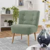 A light green accent chair is shown in a well-lit room with shelves and plants in the background. Produktbild-Vorschau