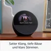 An Amazon Echo Spot smart speaker is placed on a wooden shelf, displaying music information on its screen. Produktbild-Vorschau