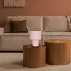 A pink table lamp sits on a wooden side table in front of a beige sofa. Produktbild-Vorschau