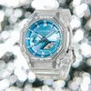 A close-up studio shot of a transparent G-Shock watch with a blue face, set against a blurred background of bokeh lights. Anteprima dell’immagine prodotto
