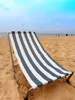 A striped beach chair sits on a sandy beach with the ocean and sky in the background. Produktbild-Vorschau