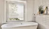 A clean, modern bathroom with a white bathtub and a window with white blinds. Produktbild-Vorschau