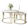 Two round coffee tables with white tops and gold chrome legs, one larger than the other, are shown against a white background. The larger table has a vase of white flowers, and the smaller table has a candle and two teacups. Produktbild-Vorschau