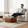 A man is relaxing on a sofa with his feet up on a pouf in a living room. Produktbild-Vorschau