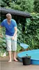 A man is cleaning a pool with a net, and a black bucket is next to the pool. Anteprima dell’immagine prodotto