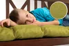 A young boy is lying on a green cushion on a wooden bench. Produktbild-Vorschau