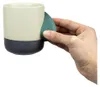 Keramiktasse "Climbing Mug Evo" von YY Vertical mit Klettergriff; beige und dunkelblau; in Hand gehalten. Podgląd zdjęcia produktu