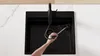 A person is cleaning a black kitchen sink with a black faucet. Produktbild-Vorschau