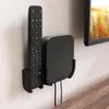 A black remote control and a black media box are mounted on a light-colored wall next to a television. Produktbild-Vorschau