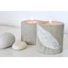 Two concrete candle holders with lit candles and smooth stones on a white surface. Produktbild-Vorschau