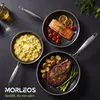 Three pans with food, including salmon, steak, and mashed potatoes, arranged on a dark surface with some scattered salt and a bottle of oil. Produktbild-Vorschau