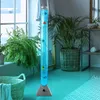A tall, illuminated bubble lamp with decorative fish is placed in a room with plants and a basket. Produktbild-Vorschau