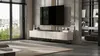 A modern living room with a TV mounted on the wall above a TV stand. Large windows with blinds are on the left, and a bookshelf is visible on the right. Produktbild-Vorschau