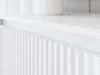 A close-up view of a white fluted cabinet door, with a white shelf above it. Voir les images du produit