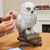A person's hands are assembling a 3D puzzle of Hedwig the owl, which is perched on a stack of books. In the background, a fireplace and a toy train are visible. Produktbild-Vorschau