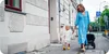 A woman and a child walking on a sidewalk next to a building, with a stroller. Produktbild-Vorschau