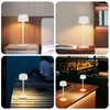 A collage of four images showing a white LED table lamp in different settings: on a nightstand, on a desk with books, on a wooden pier at night, and on a bar counter. Produktbild-Vorschau