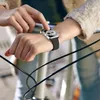 A person's hand is shown interacting with an Apple Watch on their wrist, with a bicycle in the background. Anteprima dell’immagine prodotto