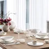 A dining table set with white tableware, glassware, and a floral arrangement. Voir les images du produit