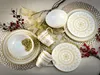A set of white and gold mandala-patterned dinnerware, including plates, bowls, and mugs, arranged on a decorative placemat with festive embellishments like berries and gold ribbon. Náhľad obrázku produktu