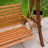 A wooden garden swing seat is shown outdoors on a patio, with grass and a planter in the background. Náhled obrázku produktu