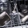 Close-up view of various metal attachments for a kitchen appliance, placed inside a dishwasher rack. Produktbild-Vorschau