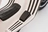 Close-up of the footrest and pedal area of a white Vespa electric scooter with black stripes. Podgląd zdjęcia produktu