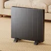 A dark gray electric heater with vertical panels stands on a striped rug next to a beige sofa. Produktbild-Vorschau