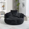 A dark gray, plush, round sofa with three pillows is shown in a well-lit room with shelves in the background. Podgląd zdjęcia produktu