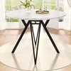 A round dining table with a marble-like top and black metal legs, set in a bright room with large windows. Produktbild-Vorschau