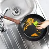 A person is cleaning a frying pan in a kitchen sink. Produktbild-Vorschau