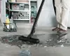 A person is vacuuming broken glass and liquid on a concrete floor in what appears to be a garage or storage area. Produktbild-Vorschau