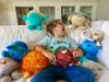 A young boy is sitting on a couch surrounded by plush planet toys. Produktbild-Vorschau