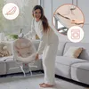 A woman is holding a baby bouncer in a living room. Produktbild-Vorschau