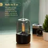 Aroma diffuser emitting mist on a wooden surface, with a camera and plant in the background. Podgląd zdjęcia produktu