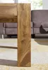 A close-up of a wooden table leg on a rug, with a sofa in the background. Produktbild-Vorschau