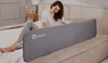 A woman is sitting on a bed next to a bed rail. Voir les images du produit